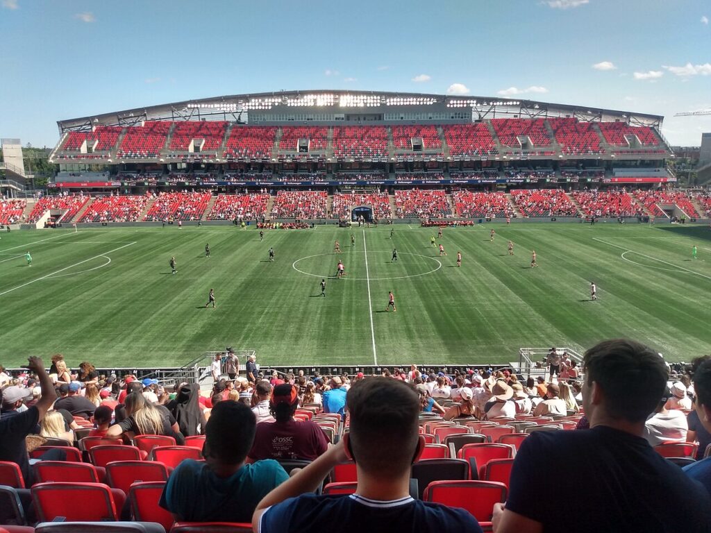 Atlético Ottawa and HFX Wanderers players on the field at TD Place moments after kick-off, with fans in the stands.