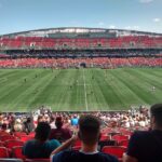 Atlético Ottawa and HFX Wanderers players on the field at TD Place moments after kick-off, with fans in the stands.