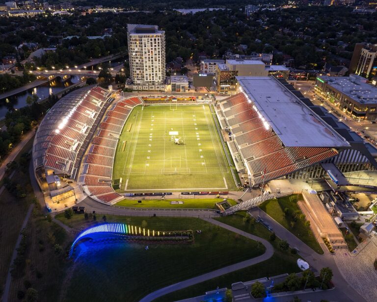 Aerial view of TD Place stadium lit up at night, with the field and stands visible.